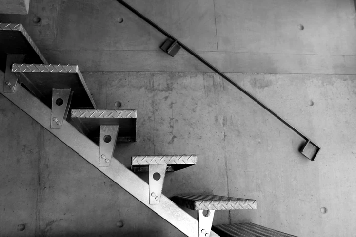 Escalier industriel en acier avec marches caillebotis et limons latéraux, fixé contre mur béton brut