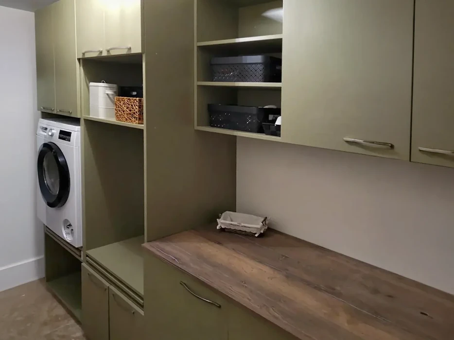 Buanderie moderne avec machine à laver encastrée, placards de rangement beiges, étagères ouvertes contenant paniers et bacs de stockage