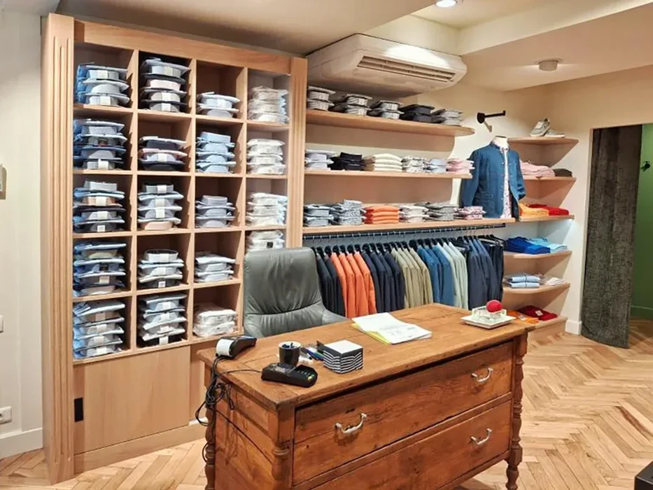 Intérieur d'une boutique de vêtements masculins avec vendeuse en chemise bleue présentant des articles