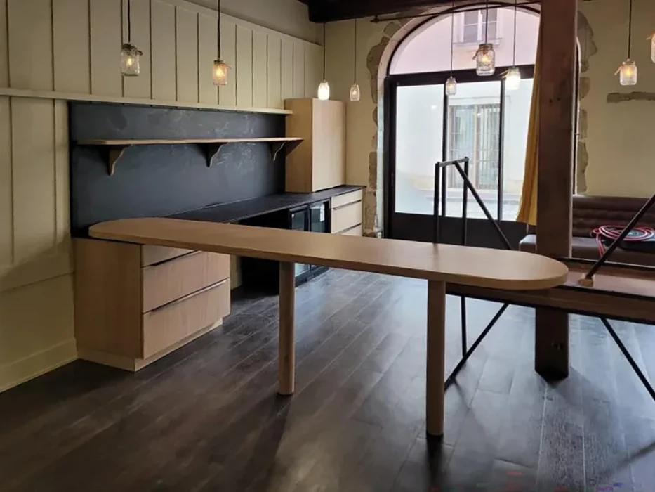 Cuisine moderne ouverte avec îlot central ovale en bois clair, façades laquées beiges, crédence ardoise noire