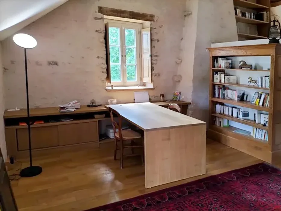 Bureau moderne en bois clair avec plan de travail rectangulaire et rangements intégrés, situé dans un espace sous combles aux murs en pierre apparente