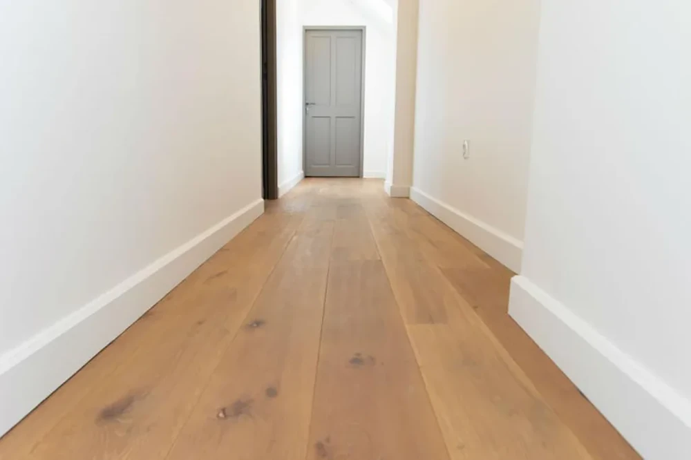 Couloir intérieur moderne avec parquet en bois naturel massif présentant des nœuds apparents, murs blancs immaculés et plinthe assortie