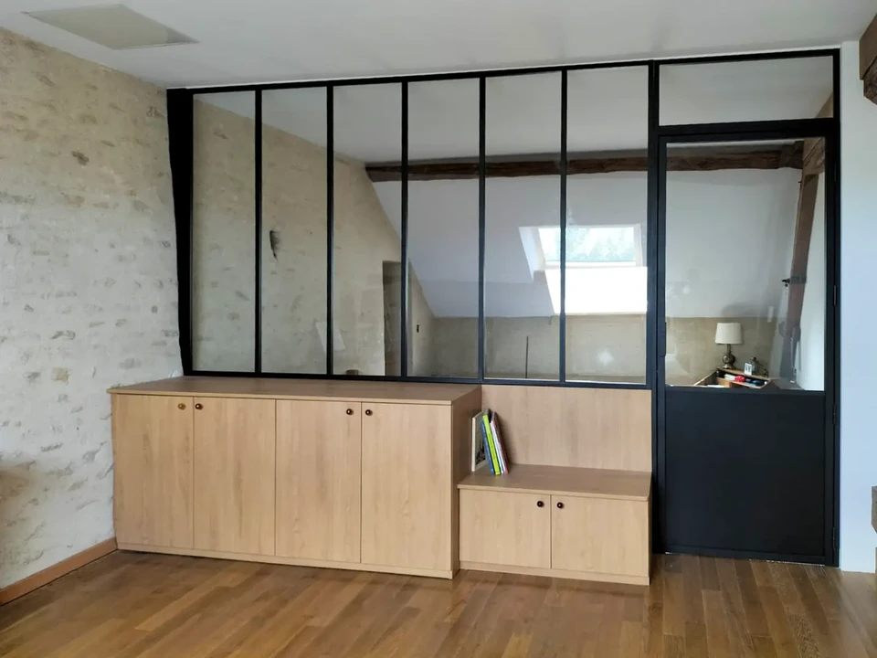 Atelier d'artisan avec établi noir central, murs en briques peintes blanches, grandes fenêtres industrielles