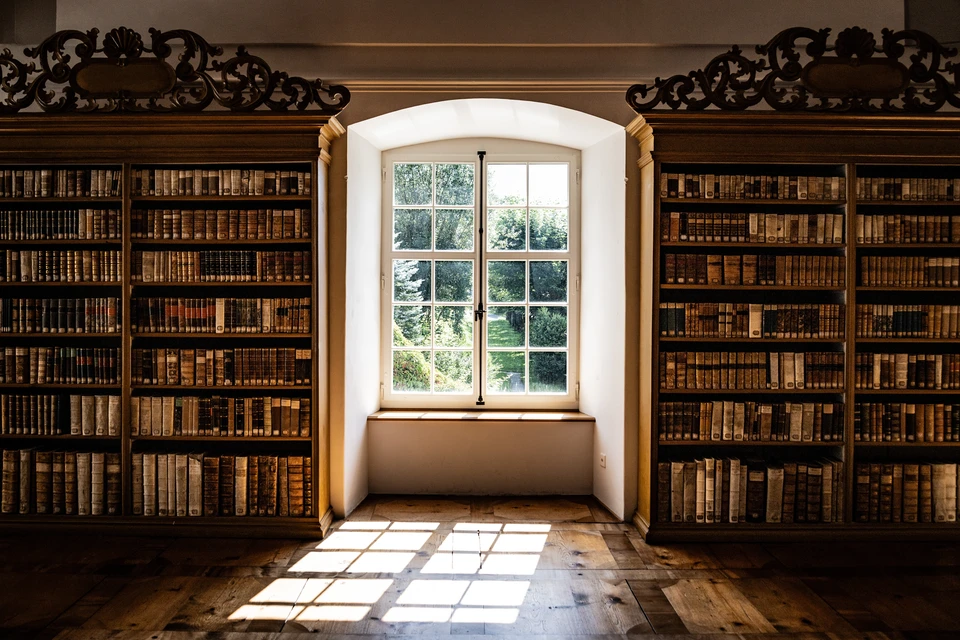 Salon moderne avec canapé futon bois et coussins noirs, bibliothèque métallique industrielle, horloge murale géante, table basse cubique marbre